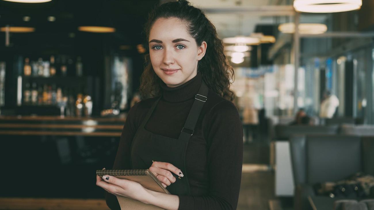 A restaurant manager in an apron holding a tablet